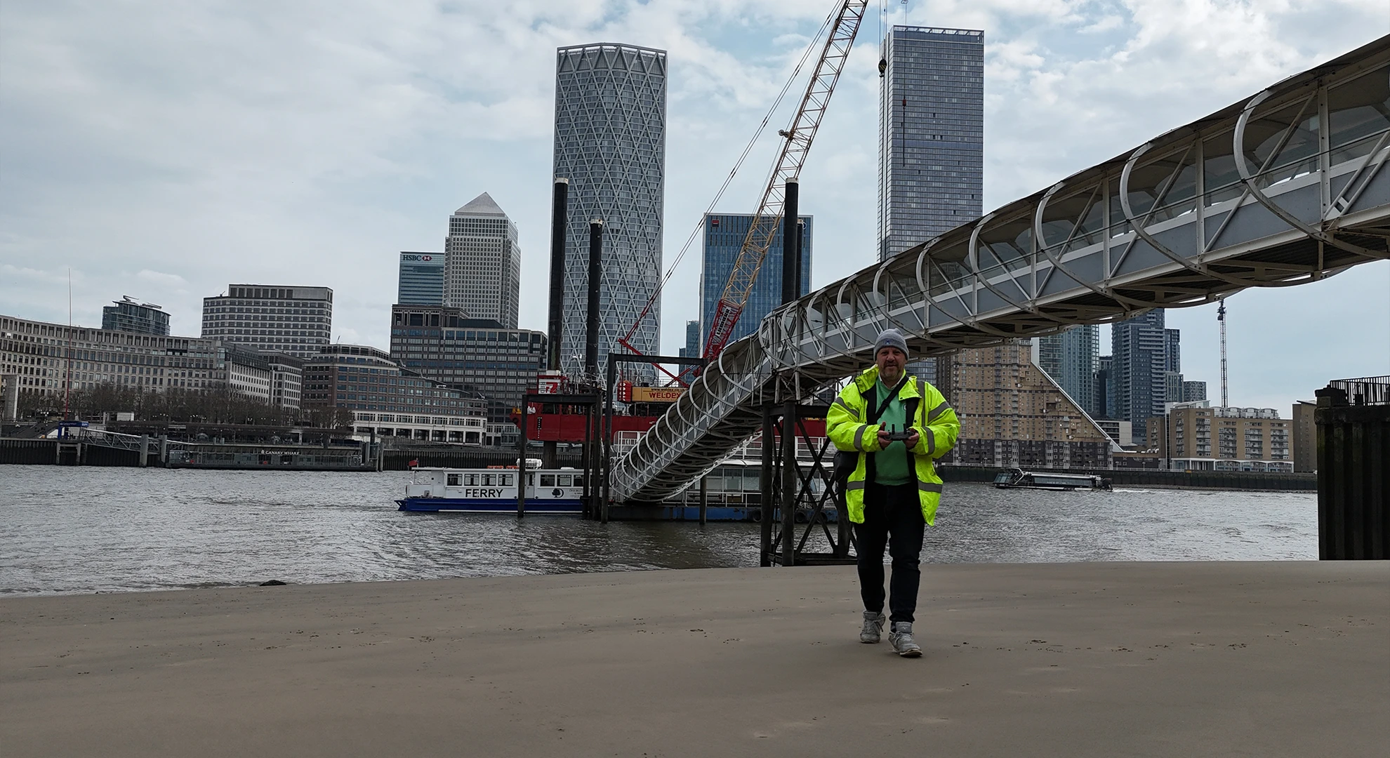Professional survey drone pilot in high-visibility jacket operating a drone controller for a commercial aerial survey.