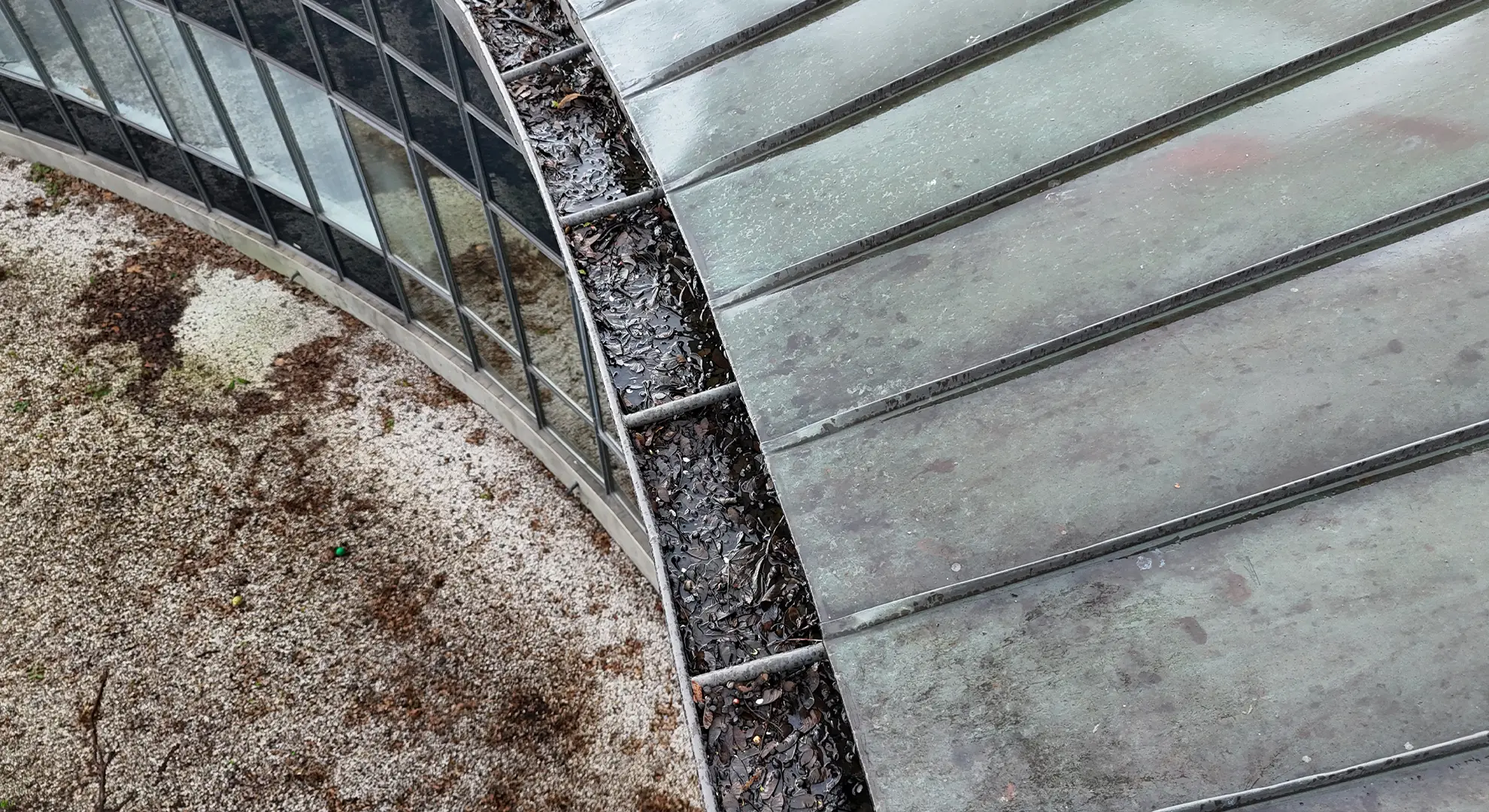 Drone inspection image of a metal roof gutter clogged with wet leaves and debris
