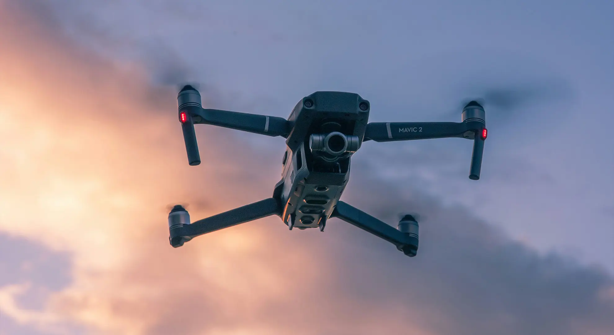 A DJI Mavic 2 drone in flight against a sunset sky