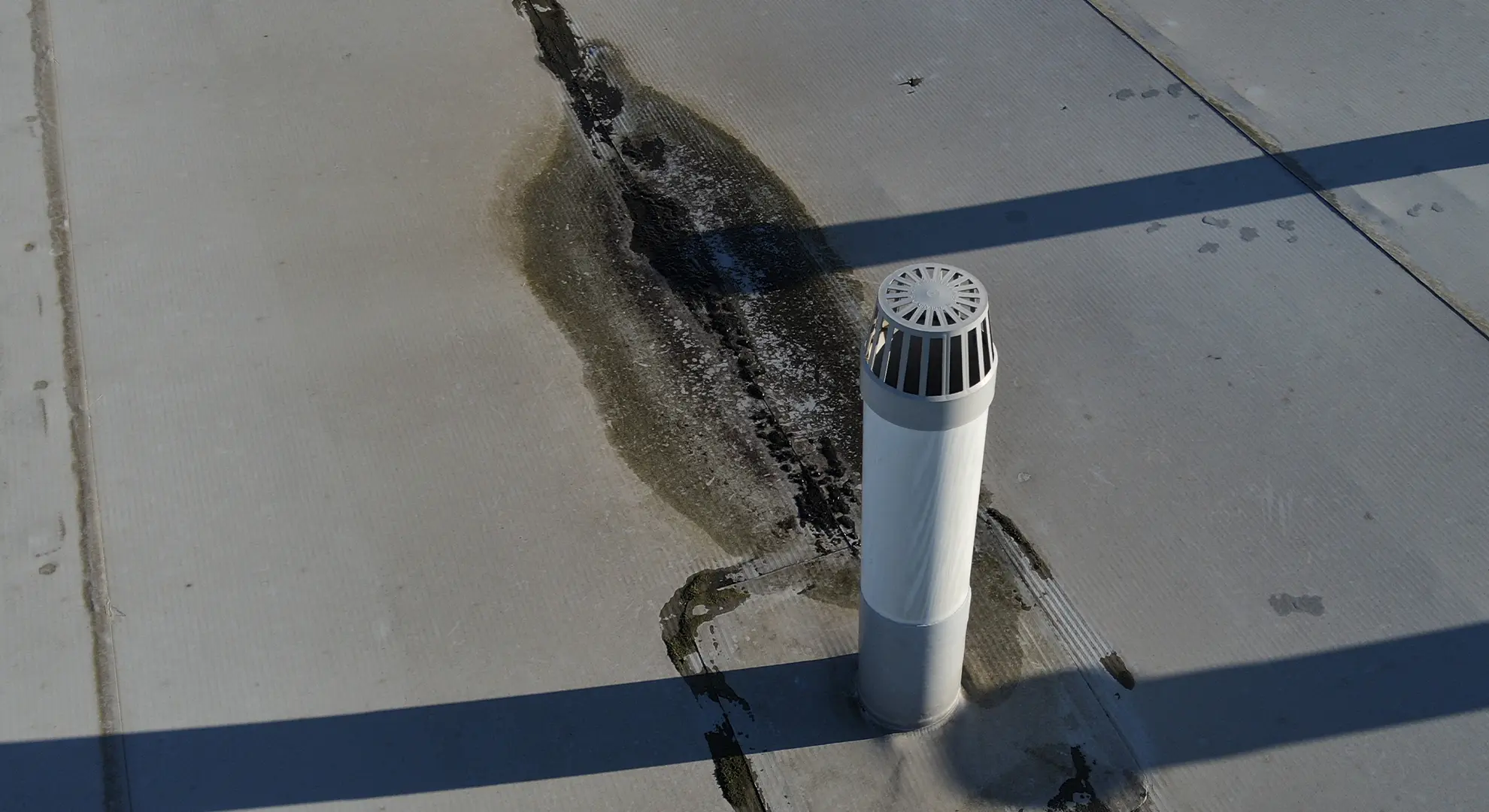 Water staining on a flat roof surface extending from the base of a white vent pipe
