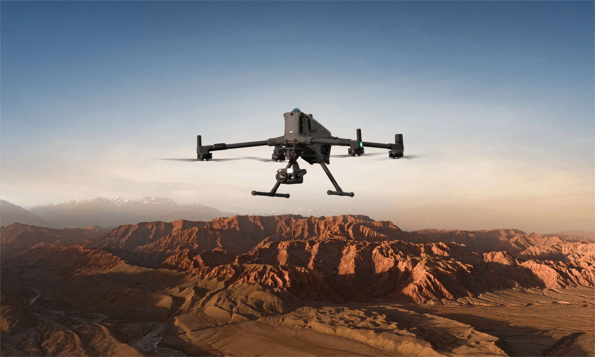 DJI Matrice 400 enterprise drone with a gimbal camera payload hovering in flight over a rugged mountain canyon landscape.