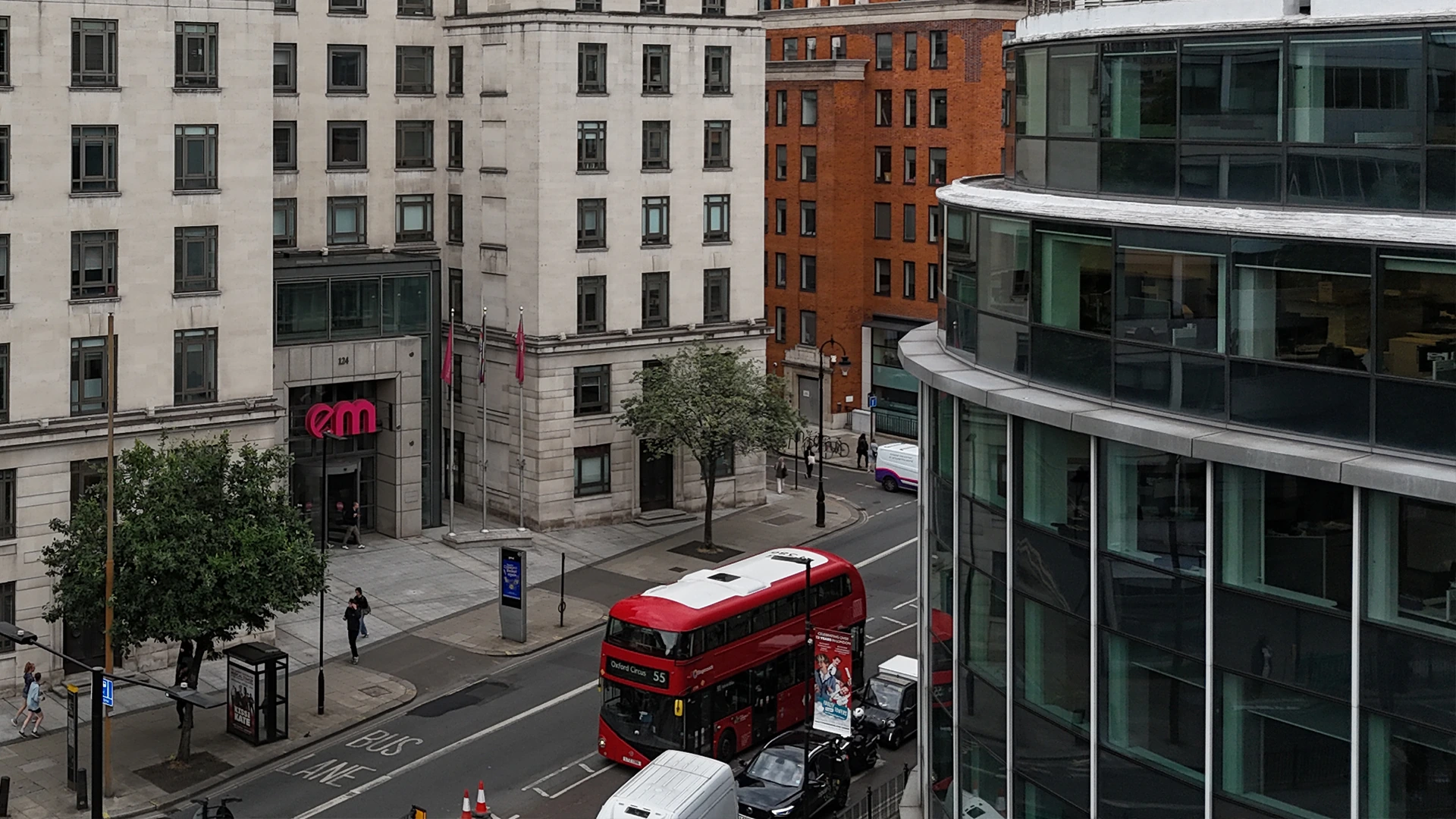 Elevated aerial drone view of commercial building facades and a red double-decker bus driving along an urban city street.