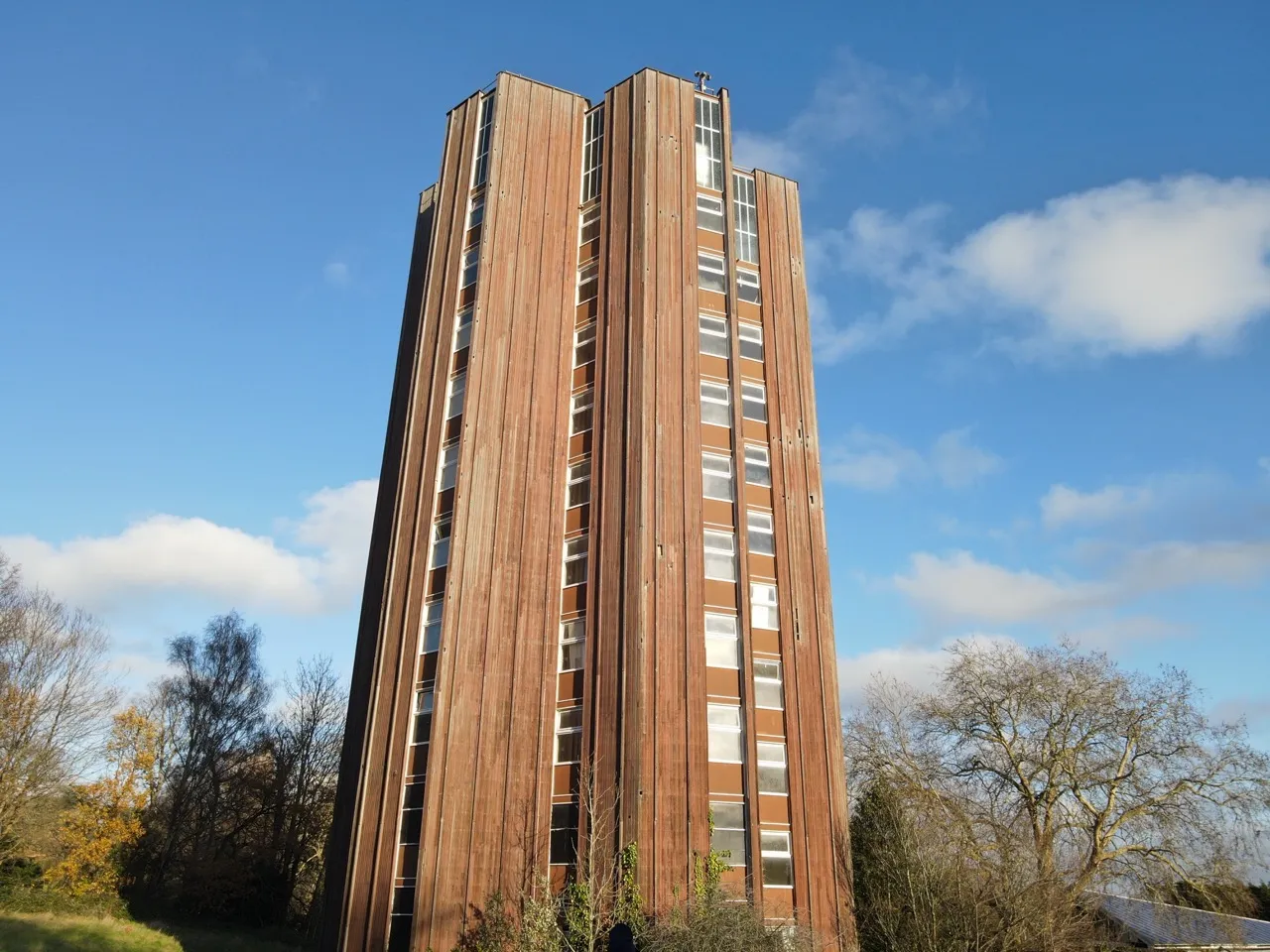 The Lodge tower block in Crystal Palace seen from ground level, with its tall brown-clad facade against a blue sky