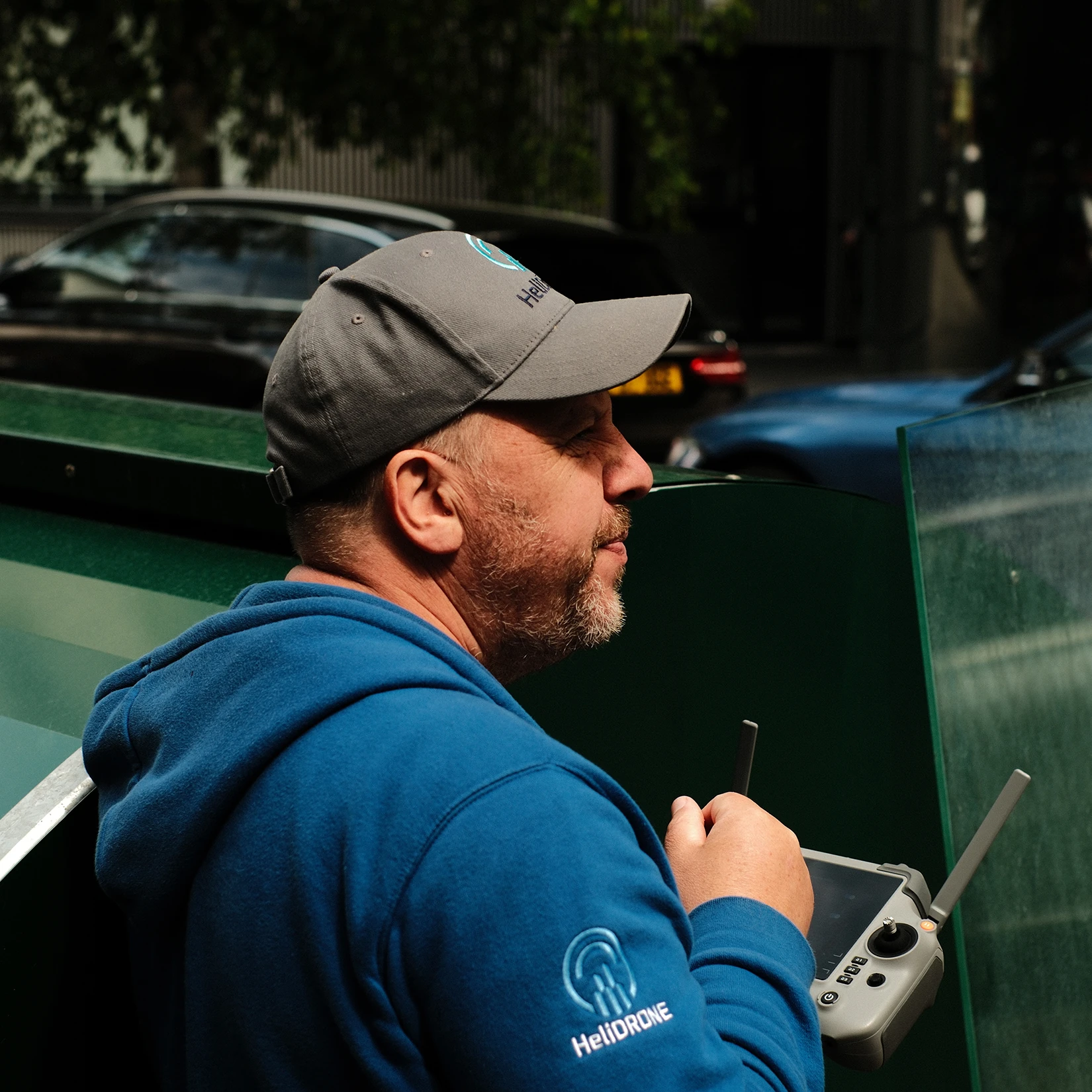 HeliDrone Surveys owner and pilot Bob McGowan wearing a blue HeliDrone hoodie and grey cap, holding a drone remote controller