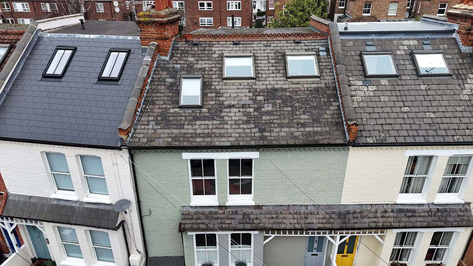 Elevated aerial drone inspection view of terraced house roofs fitted with skylights, showing contrasting newly tiled and weathered slate conditions.