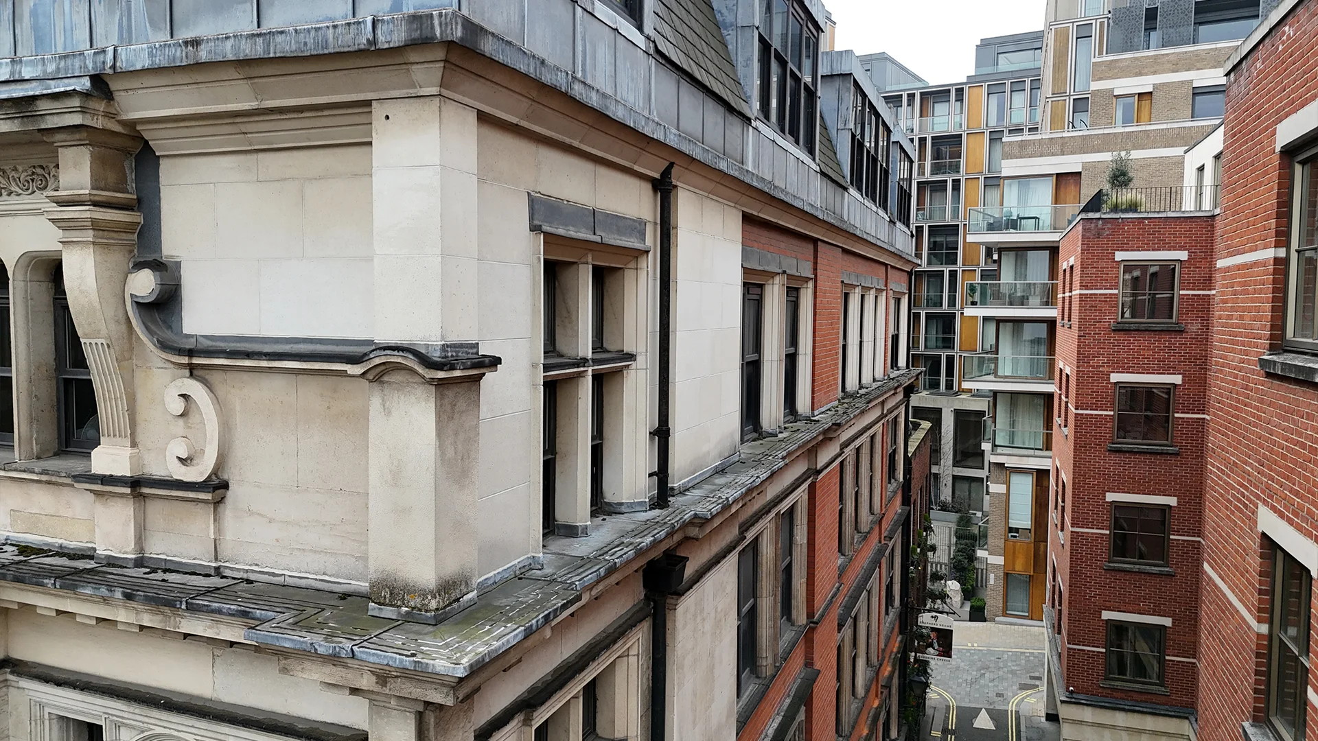 Elevated aerial drone view inspecting the stone facade, ledges, and brickwork of buildings along a narrow urban street.