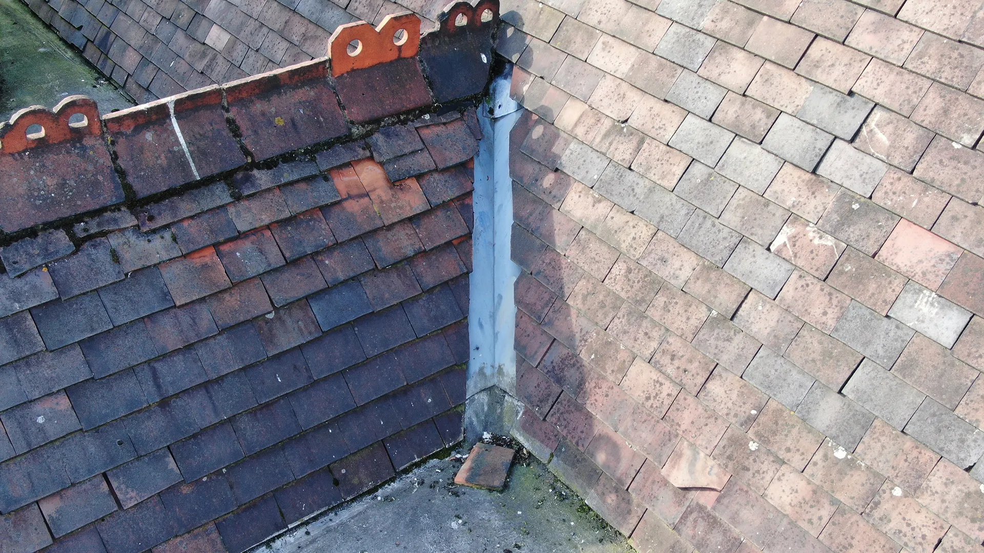 Close-up aerial drone roof inspection view showing slipped and broken tiles along a metal valley gutter.